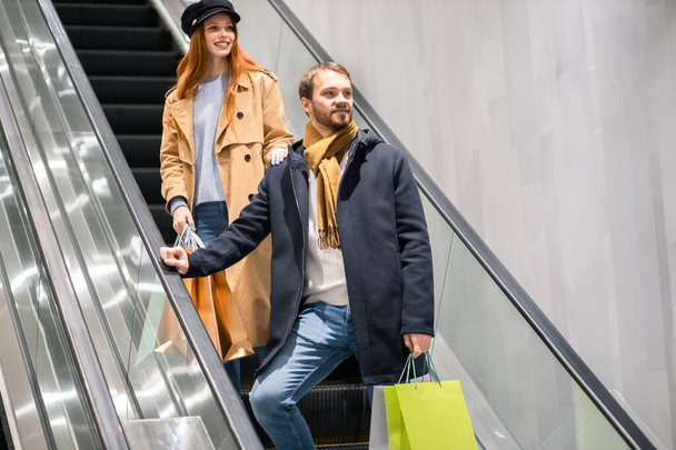 young caucasian couple together with paper bags in escalator - Fotoğraf, Görsel