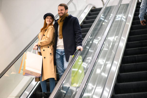 lovely caucasian couple together with paper bags in escalator - Foto, immagini