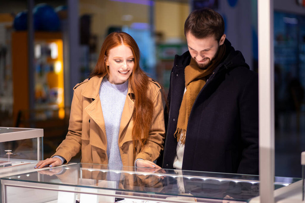 redhaired woman with male selects expensive jewelry at jewelers shop - Φωτογραφία, εικόνα