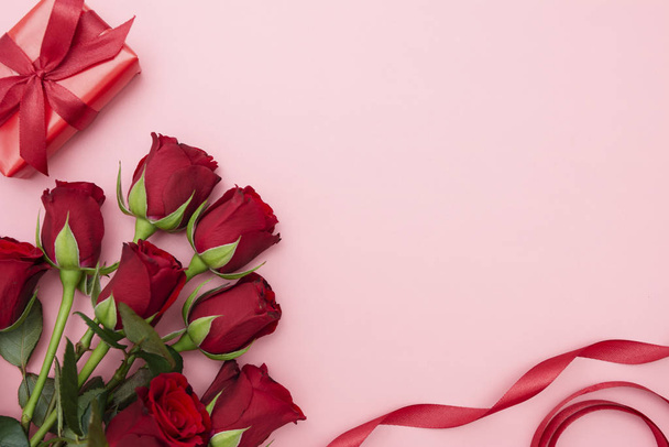 Dia dos Namorados, rosas vermelhas e caixa de presente com fita, sobre fundo vermelho flat lay, aniversário abstrato fundo com espaço de cópia
. - Foto, Imagem