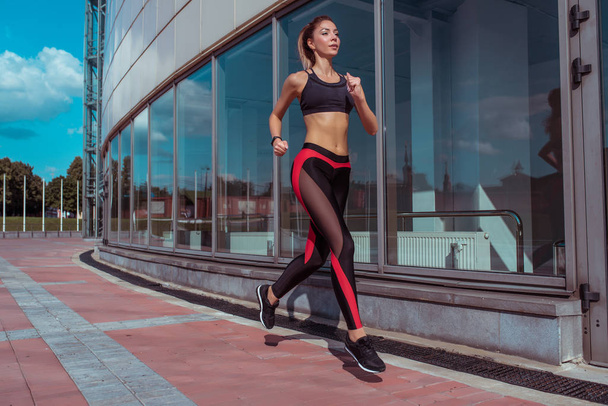 woman running young athletic in summer on jogging in city, background glass windows of building, sportswear. Athletics training, day morning. Active fitness lifestyle, free space text motivation. - Foto, Bild