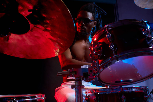 Attraente uomo africano batterista godendo suonare la batteria su sfondo scuro
 - Foto, immagini