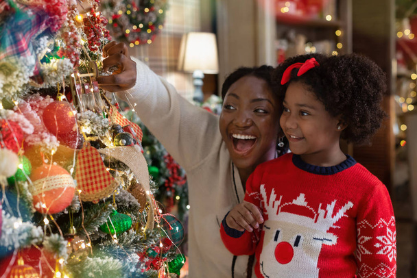 Iloinen musta äiti ja tytär katsomassa helyjä joulukuusessa
 - Valokuva, kuva