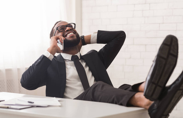 Relajado gerente negro hablando por teléfono mientras tiene descanso
 - Foto, Imagen