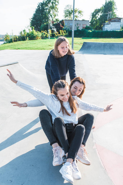 Three girls schoolgirls teenagers 13-15 years old, fall day summer city, ride skateboard. Emotions joy are fun enjoyment happy are smiling laughing, casual clothes, relaxing after school on vacation. - Foto, Imagen