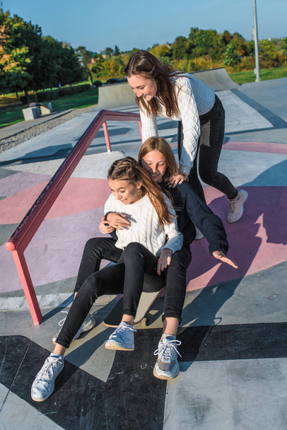 Three girls schoolgirls teenagers 13-15 years old, autumn day summer city, skateboarding. Emotions joy are fun enjoyment, happy are smiling laughing, casual clothes, relaxing after school on vacation. - Фото, изображение