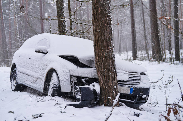 Σπασμένο αυτοκίνητο συντρίβεται σε δέντρο μετά την απώλεια ελέγχου στο ολισθηρό δρόμο σε χιονισμένο δάσος. - Φωτογραφία, εικόνα