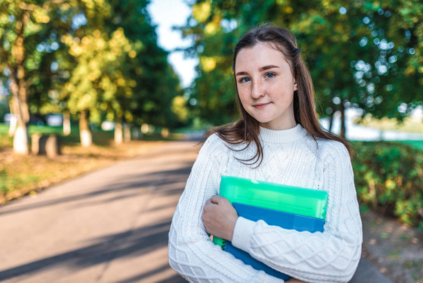 Teenager girl 14 years old autumn day summer city, hands notebooks folders with notes, happy smiling smart student, serious successful, sweater, outdoors portrait teenager schoolgirl. Free space text - Foto, Imagem