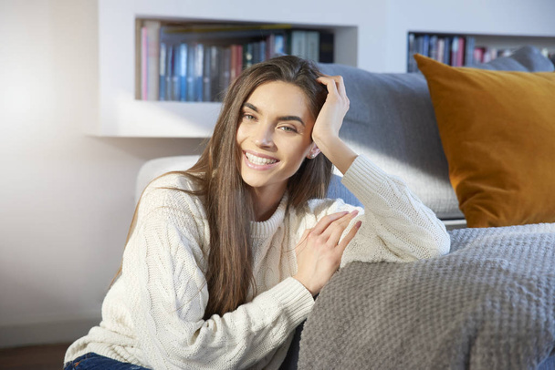 Portrait shot of a beautiful young woman wearing sweater while relaxing at home on sofa. - Valokuva, kuva