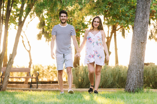 Onnellinen raskaana oleva pari kävelee puistossa ja hymyilee
 - Valokuva, kuva