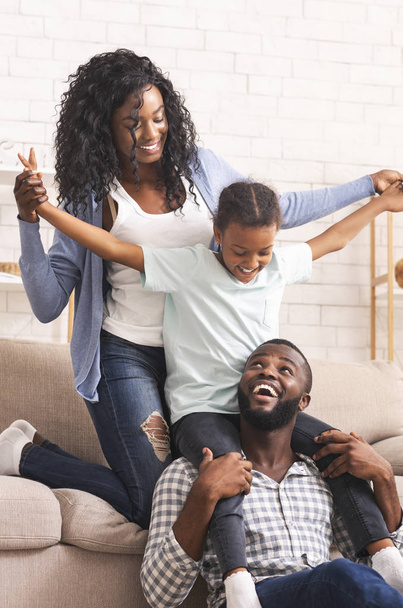 Joyful afro parents and their little daughter having fun at home - Foto, imagen