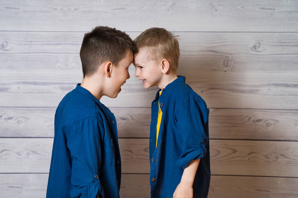 Portrait of two brothers standing head to head in studio. Boys wearing the same clothes posing together isolated on wooden background. Selective focus. - Zdjęcie, obraz