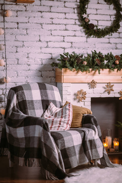 Armchair covered with a cozy blanket, standing near the fireplace decorated with a Christmas garland. - 写真・画像
