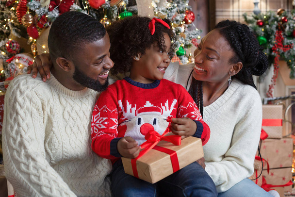 Petite fille afro ouvrant boîte cadeau de Noël avec ses parents
 - Photo, image