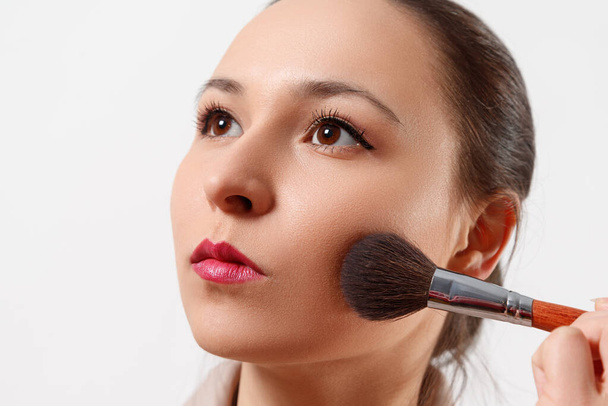 a young woman puts makeup on her face with a brush. on white background. - Фото, изображение