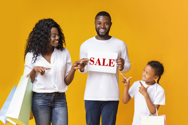 Familia negra feliz de tres señalando la hoja con la inscripción de la venta
 - Foto, imagen