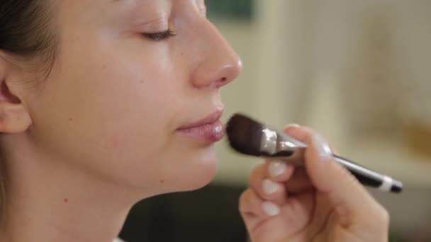 Professionele make-up kunstenaar brengt foundation cream op klanten gezicht met borstel. - Video
