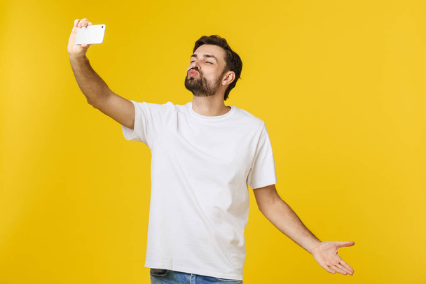 Крупный план молодого красивого мужчины, смотрящего на смартфон и делающего селфи. изолировать на желтом фоне
. - Фото, изображение