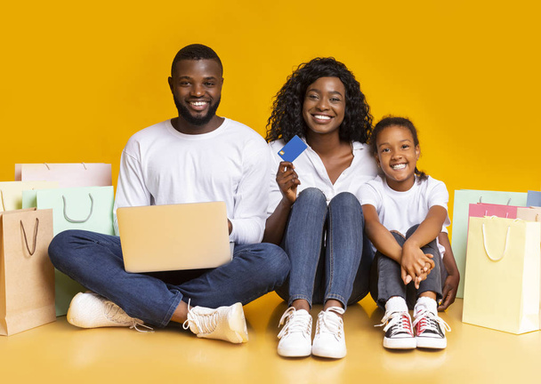 Joyful afro family with laptop, credit card and shopping bags. - Φωτογραφία, εικόνα