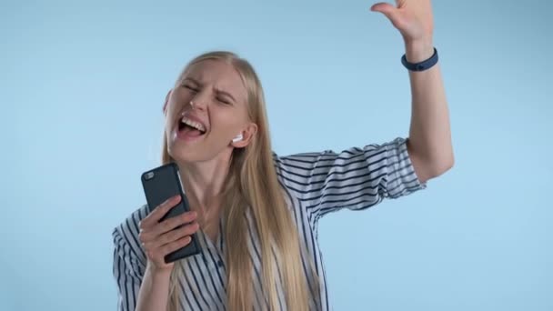 jong blond vrouw getting high terwijl het luisteren naar de muziek en zingen op blauwe achtergrond - Video