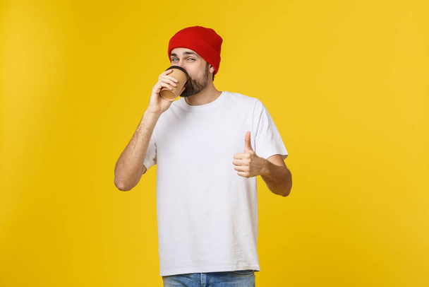 Mann auf isolierten lebendigen gelben Farbe nimmt einen Kaffee in Take-away-Pappbecher und lächelt, weil er den Tag gut beginnen wird. - Foto, Bild