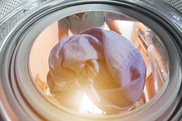 A man or woman throws dirty Laundry in the wash, look from the inside of the washing machine - Photo, Image