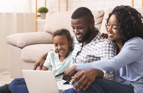 Iloinen afrikkalainen amerikkalainen perhe käyttää kannettavaa tietokonetta kotona yhdessä
 - Valokuva, kuva