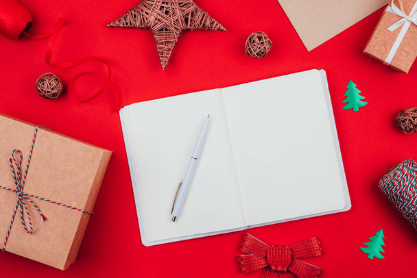 Blank notebook, pen, craft gift boxes, envelope, red bow, clew of tricolor rope, ribbon and decorations over red festive background. New year planning. - Fotoğraf, Görsel