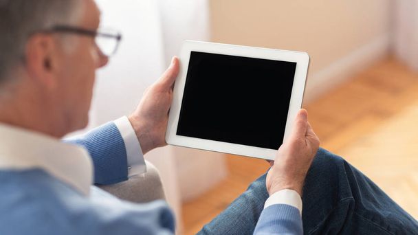 Nierozpoznawalny mężczyzna w podeszłym wieku korzystający z tabletu siedzącego w domu, panoramy, makiety - Zdjęcie, obraz