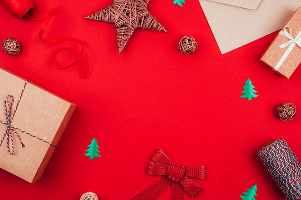 Ambachtelijke geschenkdozen, enveloppe, rode strik, strik van tricolor touw, lint en decoraties over rode feestelijke achtergrond. - Foto, afbeelding