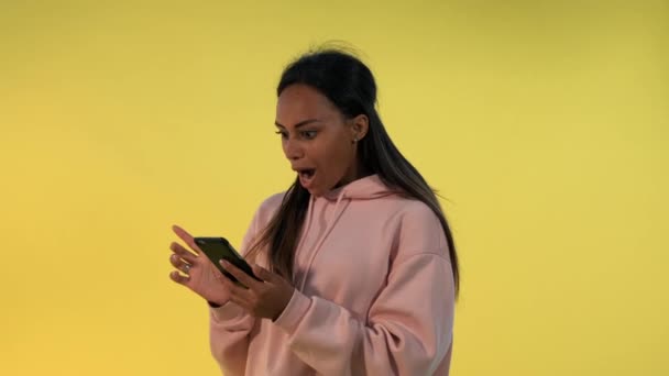 Ładna czarna kobieta znajduje coś niesamowitego surfując po Internecie na smartfonie - Materiał filmowy, wideo