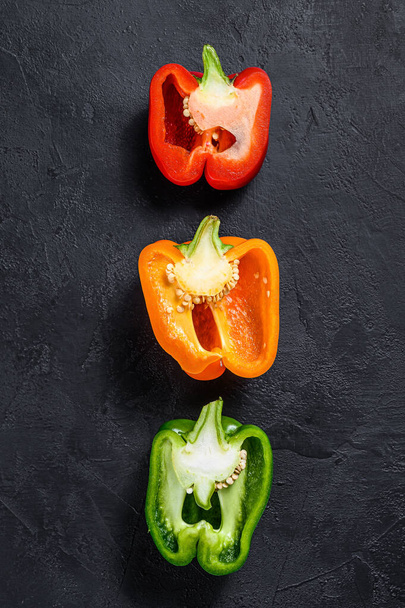 Three cut orange, green and red sweet peppers. Black background. Top view. Space for text - Foto, Bild