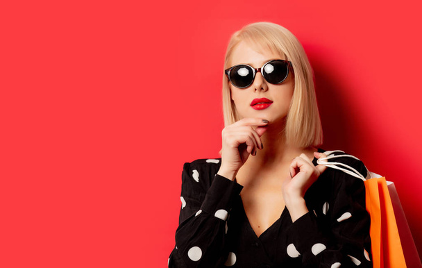 Stile ragazza bionda in occhiali da sole con borse della spesa sul retro rosso
 - Foto, immagini