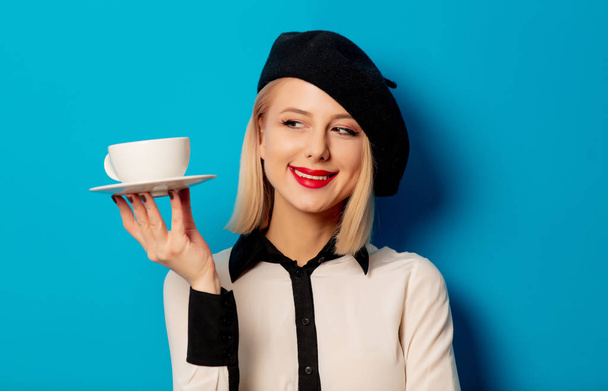 gyönyörű francia nő svájcisapkában tartja fehér csésze kávét - Fotó, kép