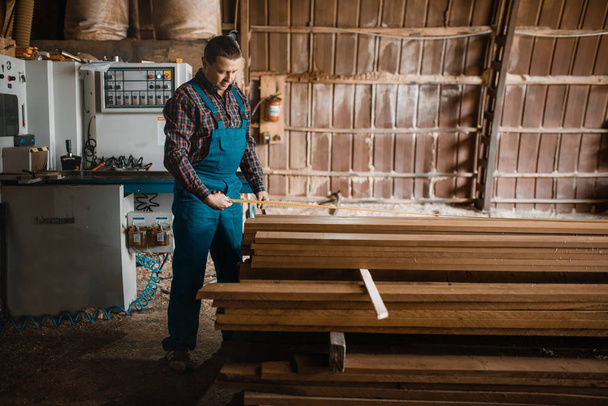 Falegname con tavole di misura a nastro, macchina per la lavorazione del legno su sfondo, industria del legno, falegnameria. Lavorazione del legno in fabbrica, segatura forestale in cantiere
 - Foto, immagini