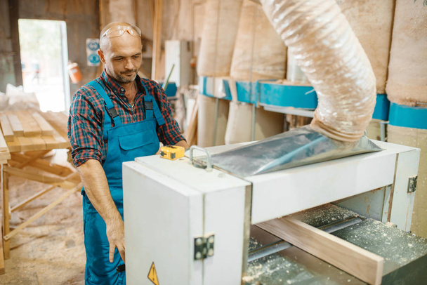 Ο ξυλουργός δουλεύει σε μηχανή αεροπλάνων, ξυλουργική, ξυλουργική, ξυλουργική. Επεξεργασία ξύλου σε εργοστάσιο επίπλων - Φωτογραφία, εικόνα