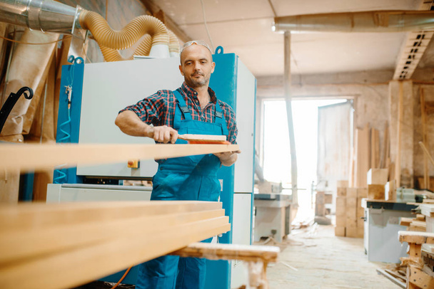 Carpenter processes board on plane machine, woodworking, lumber industry, carpentry. Wood processing on furniture factory, production of products of natural materials - Photo, Image