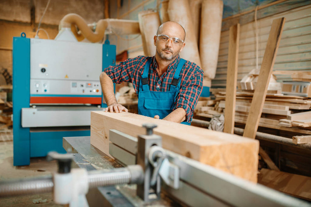 Carpintero procesa viga de madera en la máquina plana, carpintería, industria de la madera, carpintería. Procesamiento de madera en fábrica de muebles
 - Foto, Imagen