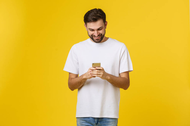 Хорошие новости от друга. Уверенный молодой красивый мужчина в джинсовой рубашке держит смартфон на желтом фоне
 - Фото, изображение
