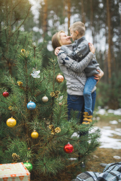 Christmas tree balls on a natural pine branchs in the winter forest. Mother and son hugging on the background. Concept of Christmas, New Year and winter Xmas holidays, background, texture - Photo, image