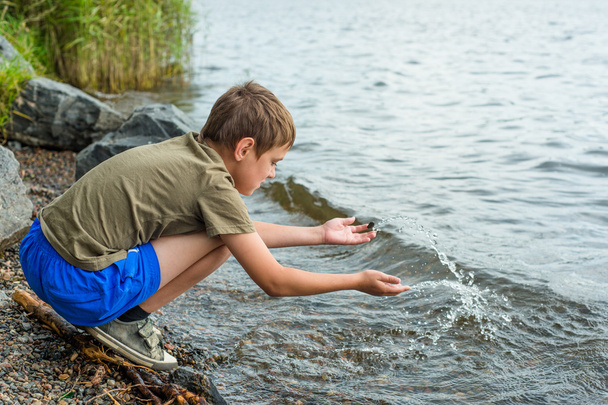 Nahaufnahme Porträt eines ernsthaften kleinen Jungen, der am Fluss sitzt - Foto, Bild