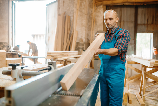Carpenter with board near plane machine, woodworking, lumber industry, carpentry. Wood processing on furniture factory, production of products of natural materials - Photo, Image