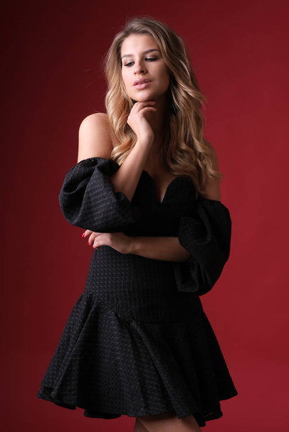 Beautiful glamour blonde model in black dress on red background. - Foto, Imagen