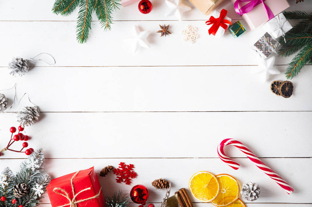 Beautiful Christmas composition on wooden white background with Christmas gift boxes, snowy fir branches, conifer cones, cinnamon dried fruits, holiday decoration, caramel stick. New Year. Top view, copy space. - 写真・画像