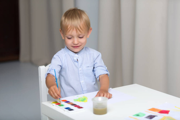 Cute little boy paints with watercolors while sitting at the tab - Foto, imagen