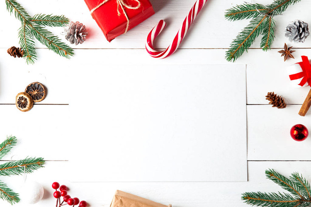 Beautiful Christmas composition on wooden white background. Empty card with Christmas present boxes, snowy fir branches, conifer cones, caramel stick, gift. New Year. Top view, copy space. - Foto, imagen