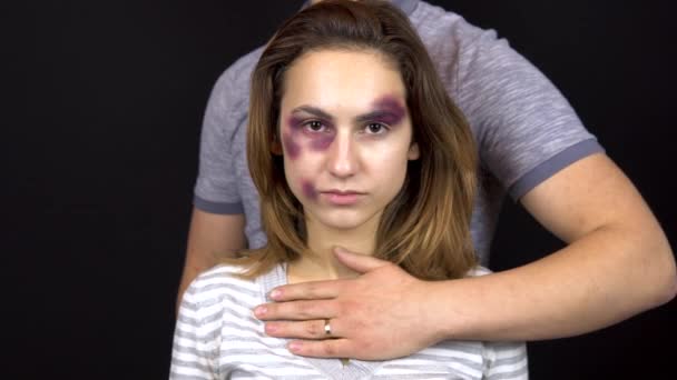 Ein junger Mann streichelt eine junge Frau. eine Frau mit blauen Flecken im Gesicht. Streit in einer jungen Familie. Häusliche Gewalt. auf schwarzem Hintergrund - Filmmaterial, Video