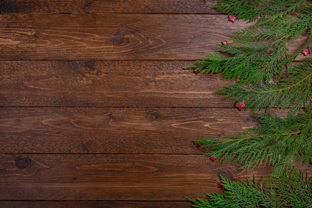 Fondo decorativo plano de Navidad o Año Nuevo: ramas de ciprés y pequeñas estrellas rojas, sobre fondo de madera oscura. maqueta de marco de vista superior con espacio de copia
. - Foto, Imagen