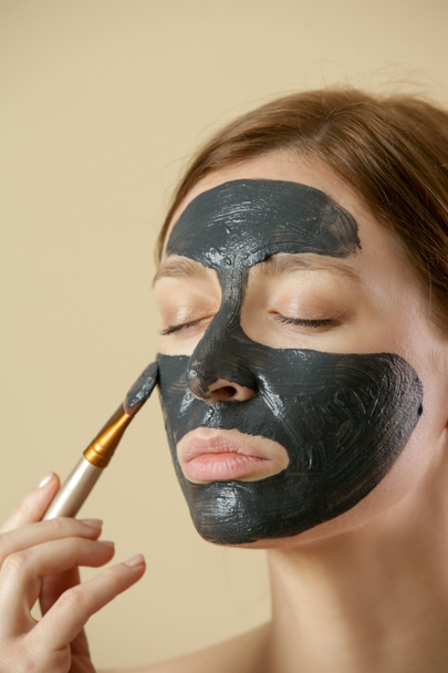 Charcoal face mask or black clay mud. Beautiful woman is applying purifying black mask on her face, close up studio shot. Home spa natural cosmetic concept. - Fotografie, Obrázek