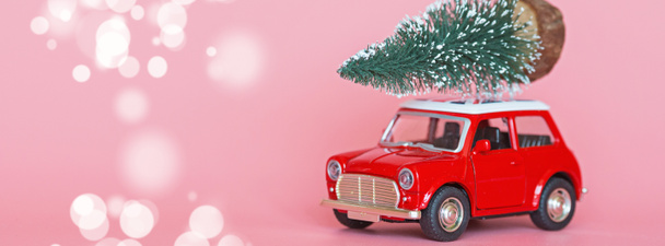 Червоний іграшковий автомобіль з ялинкою на даху на фоні рожевого паперу. Зимова доставка, Різдво, щаслива концепція святкування Нового 2020 року. вітальна листівка, макет
 - Фото, зображення